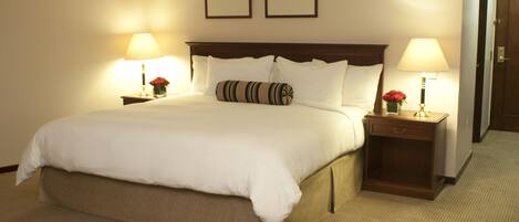 A neatly made bed with white linens, two bedside tables with lamps, and framed pictures on the wall.