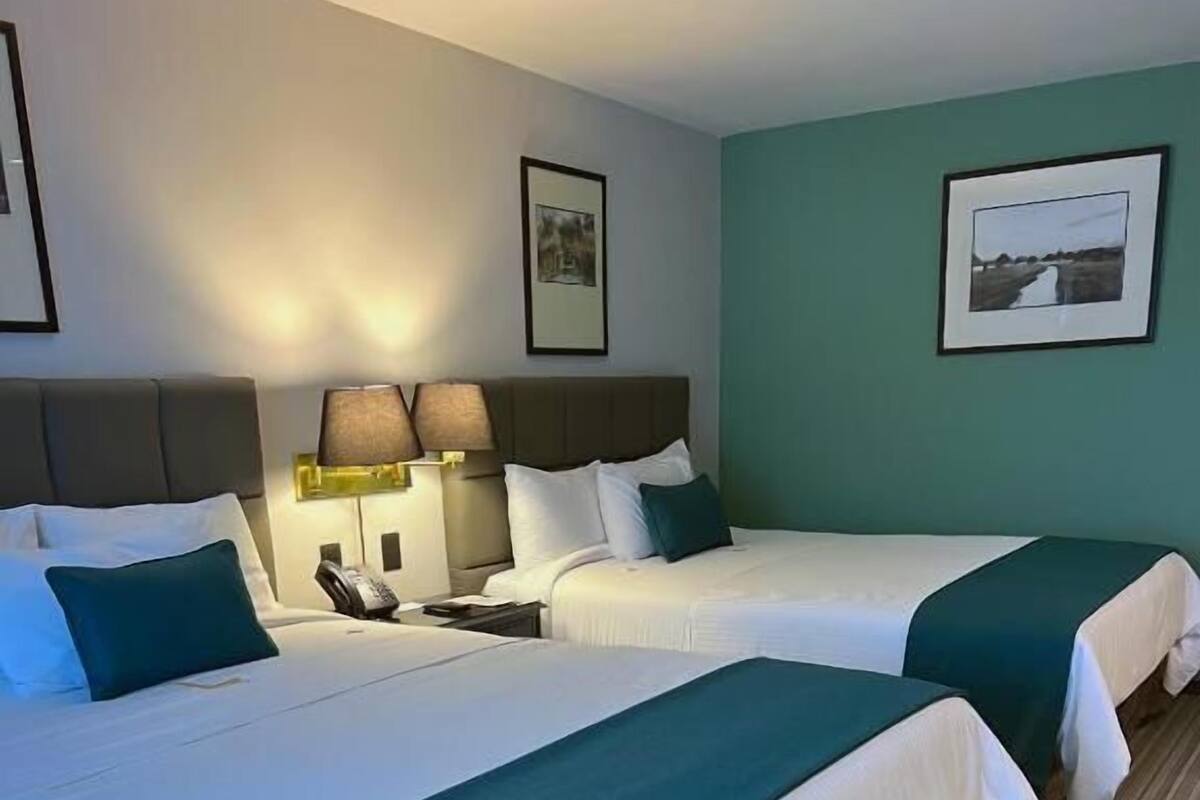 Ein Hotelzimmer mit zwei Betten, einem Nachttisch mit Lampen und gerahmten Bildern an den Wänden.
