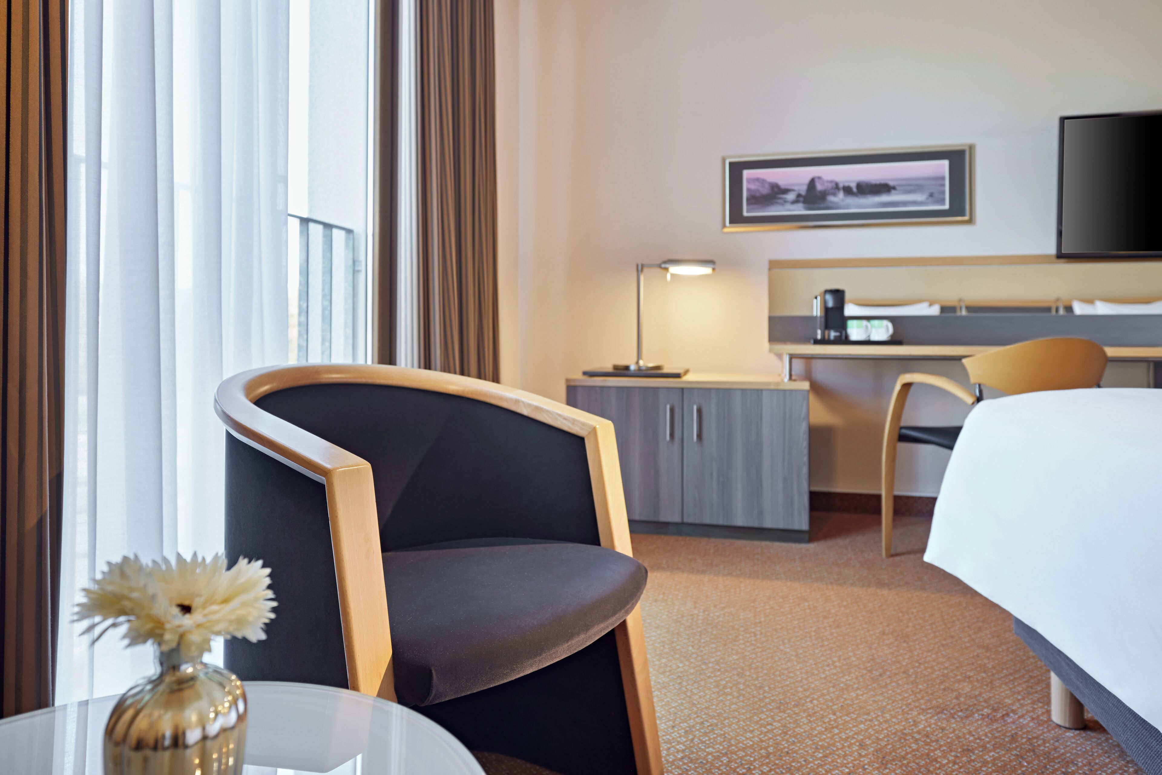 A hotel room with a bed, a desk, a chair, a lamp, and a picture on the wall.