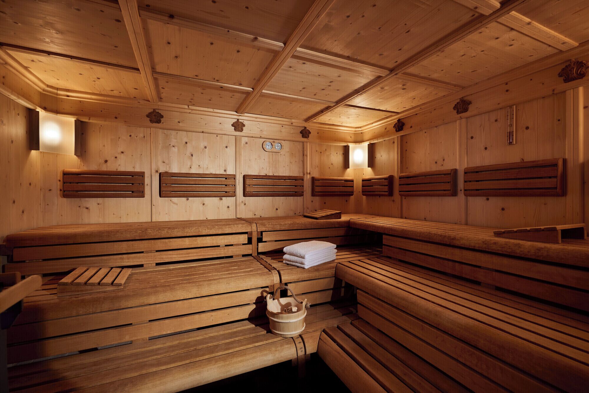 A wooden sauna with benches and benches with headrests, a wooden bucket, and a towel stack.