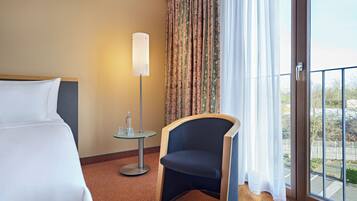 Una habitación de hotel con cama, una silla, una mesa con lámpara y vistas a través de una ventana.