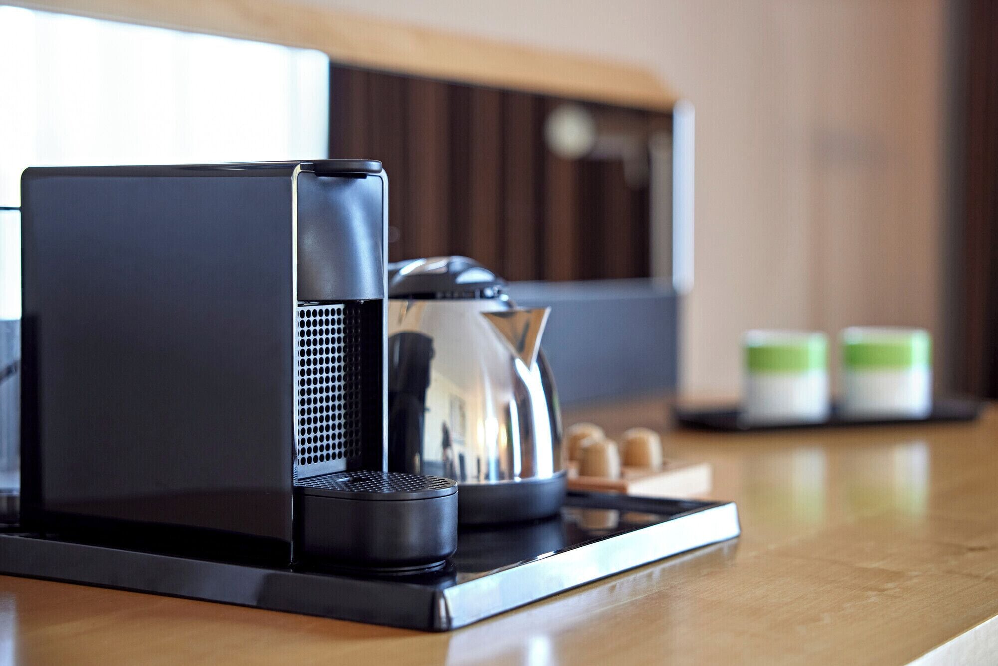 Una cocina moderna con cafetera, hervidor y una pequeña mesa con tazas y recipientes.