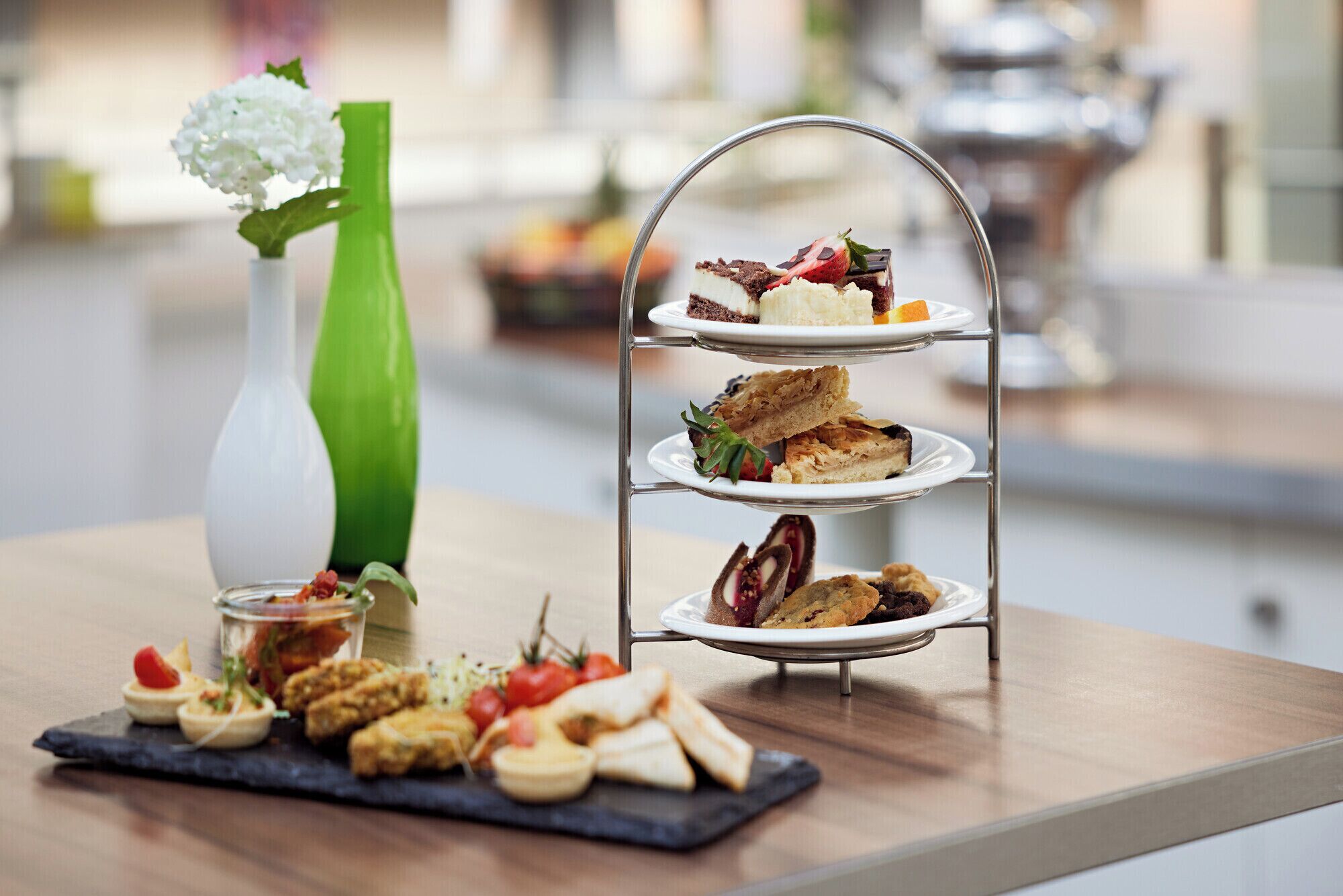 A three-tiered dessert stand with various pastries and a small vase with white flowers on a table.