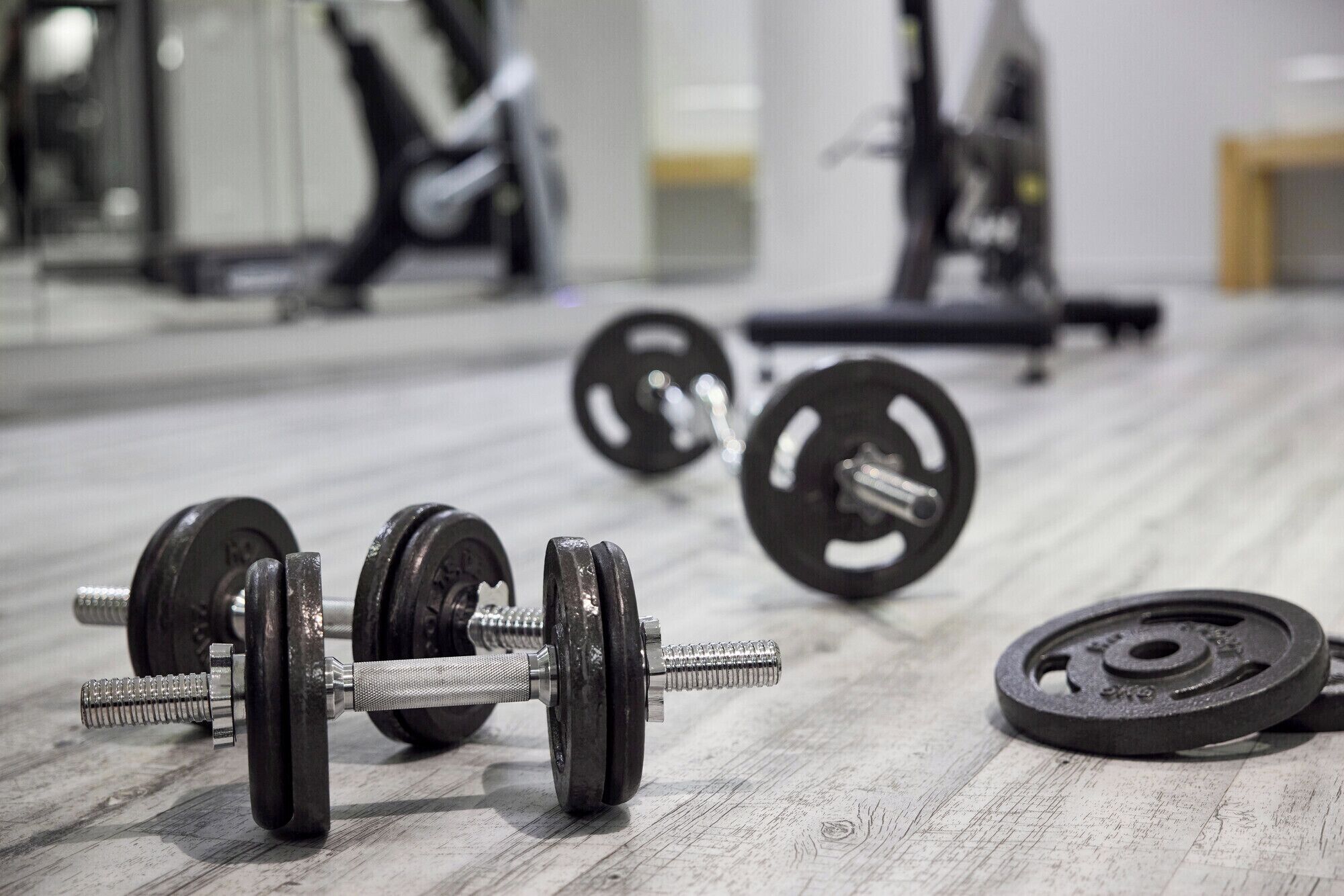 A gym with weightlifting equipment, including dumbbells and barbells, on a wooden floor.