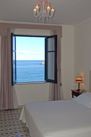 Una camera d'albergo con un letto, una finestra con tende, un lampadario e un comodino con una lampada.