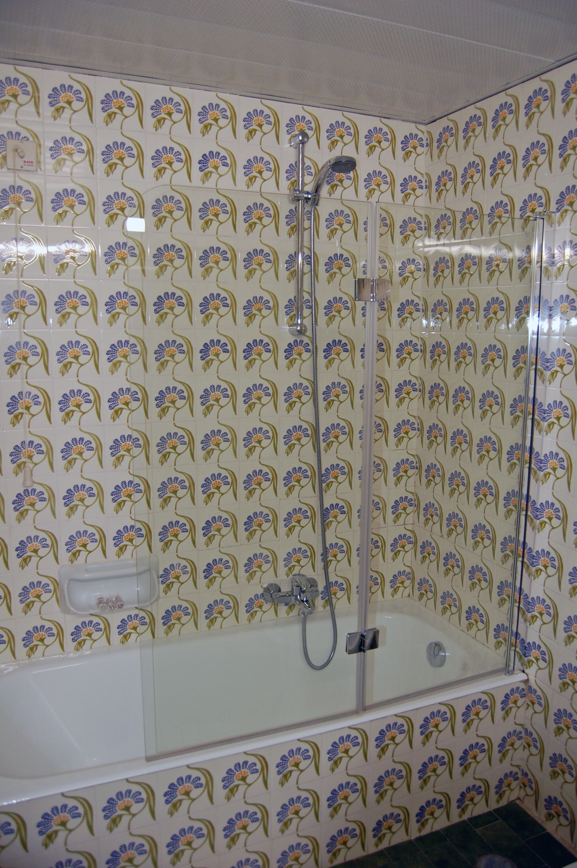 A bathroom with floral patterned tiles, a glass-enclosed shower, and a white bathtub.