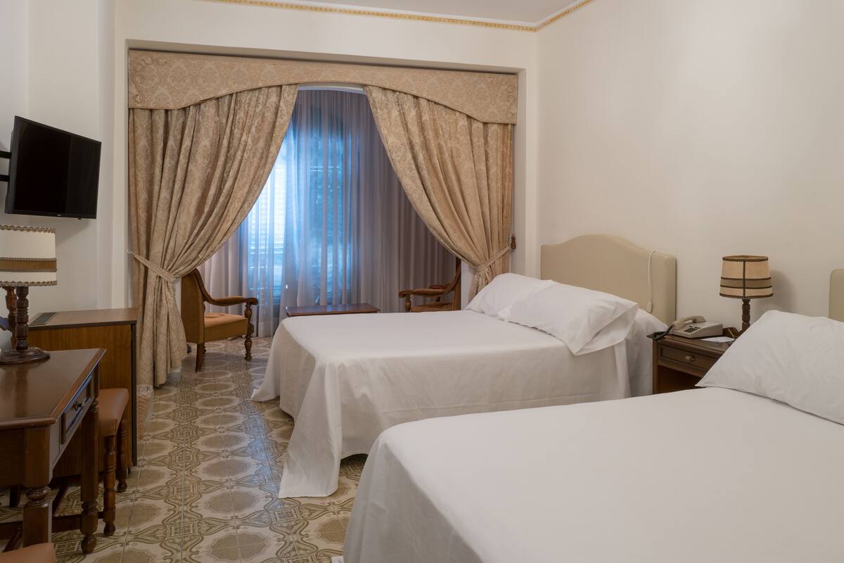 Habitación de hotel con dos camas, un escritorio, una silla, un televisor y una ventana con cortinas.