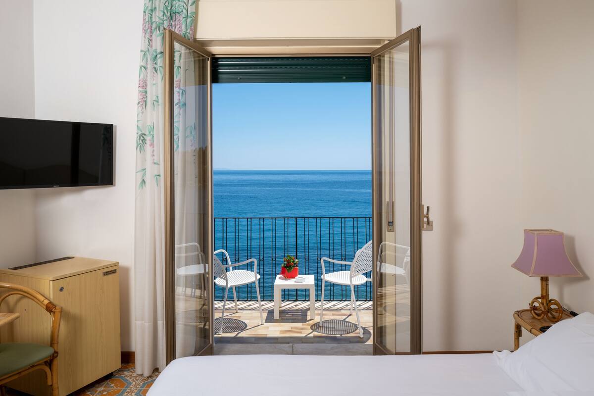 Una habitación de hotel con balcón, cama, televisor, escritorio y una silla.