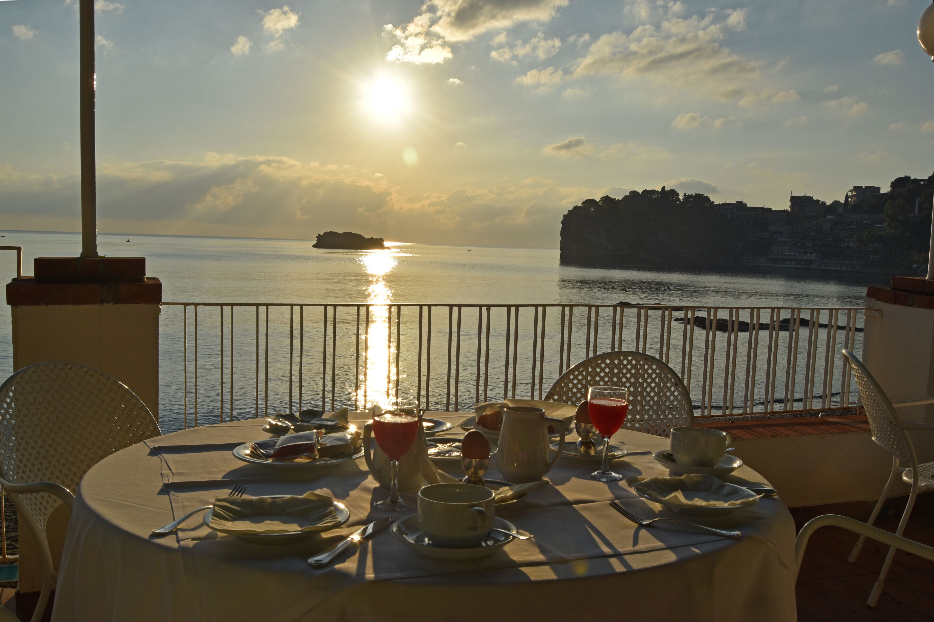 Mesa posta para o pequeno-almoço com vista para o mar e uma ilha ao longe.