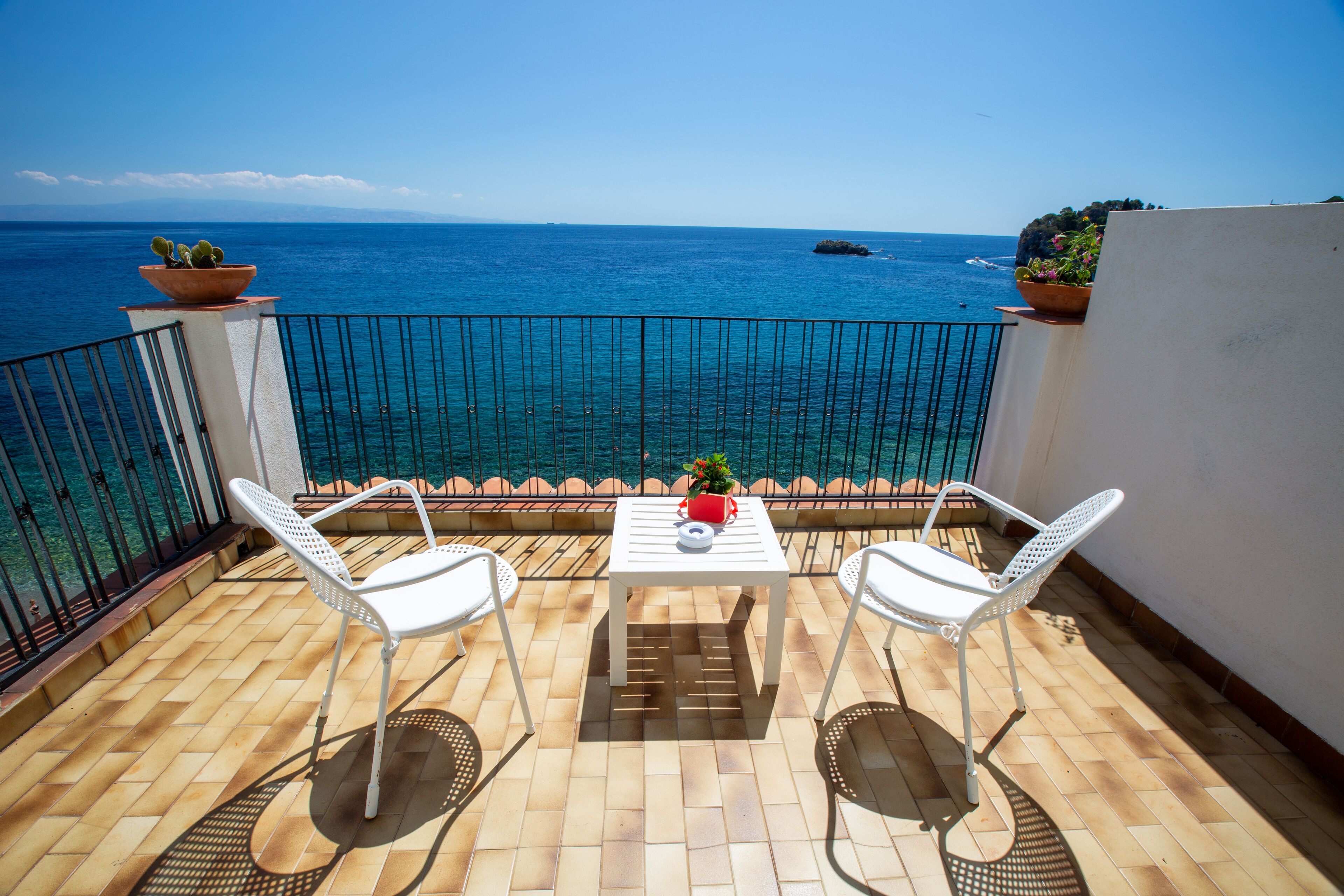 A balcony with two white chairs and a table, overlooking a clear blue sea.