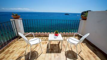 A balcony with two white chairs and a table, overlooking a clear blue sea.