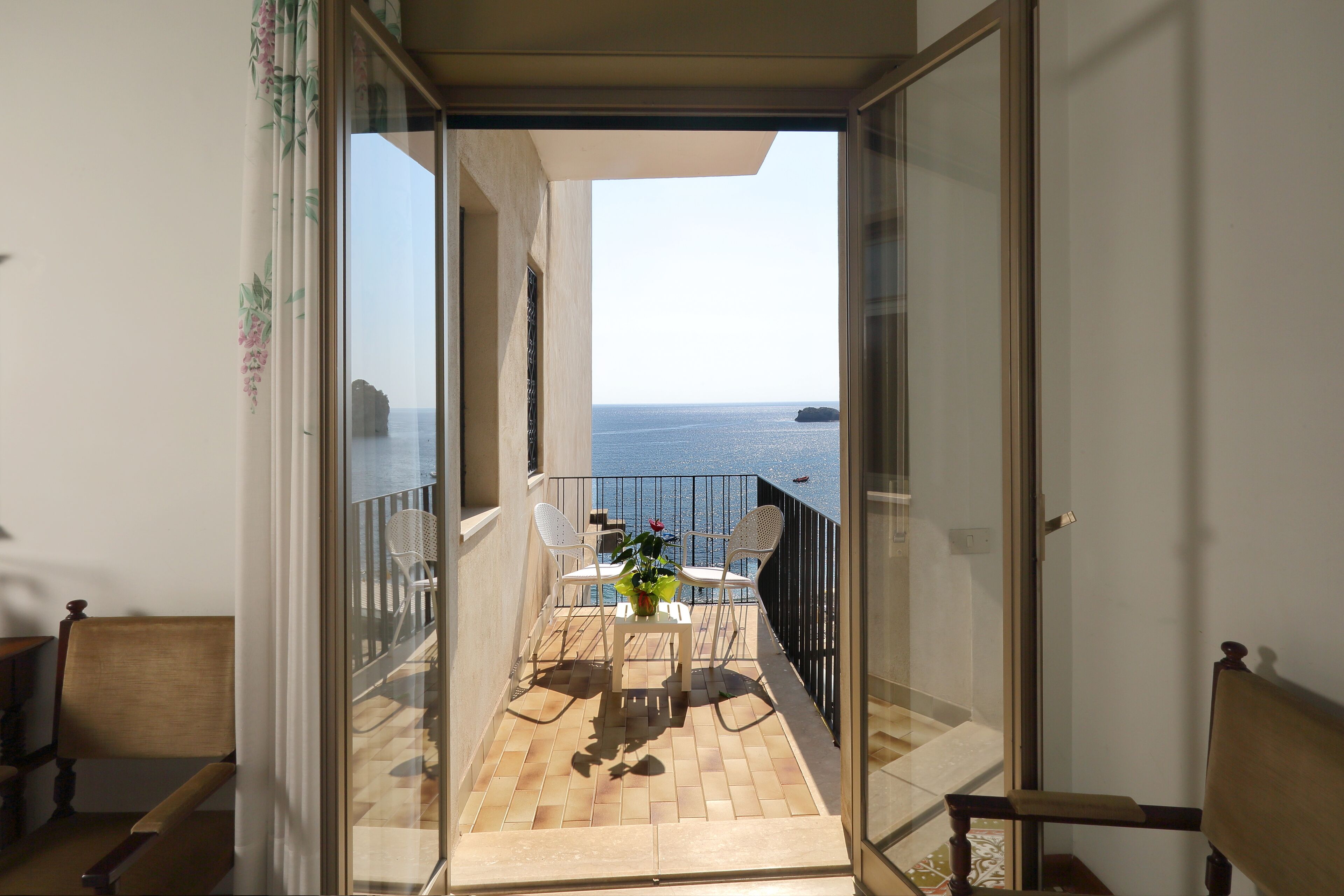 A balcony with a view of the sea, a table with chairs, and a potted plant.