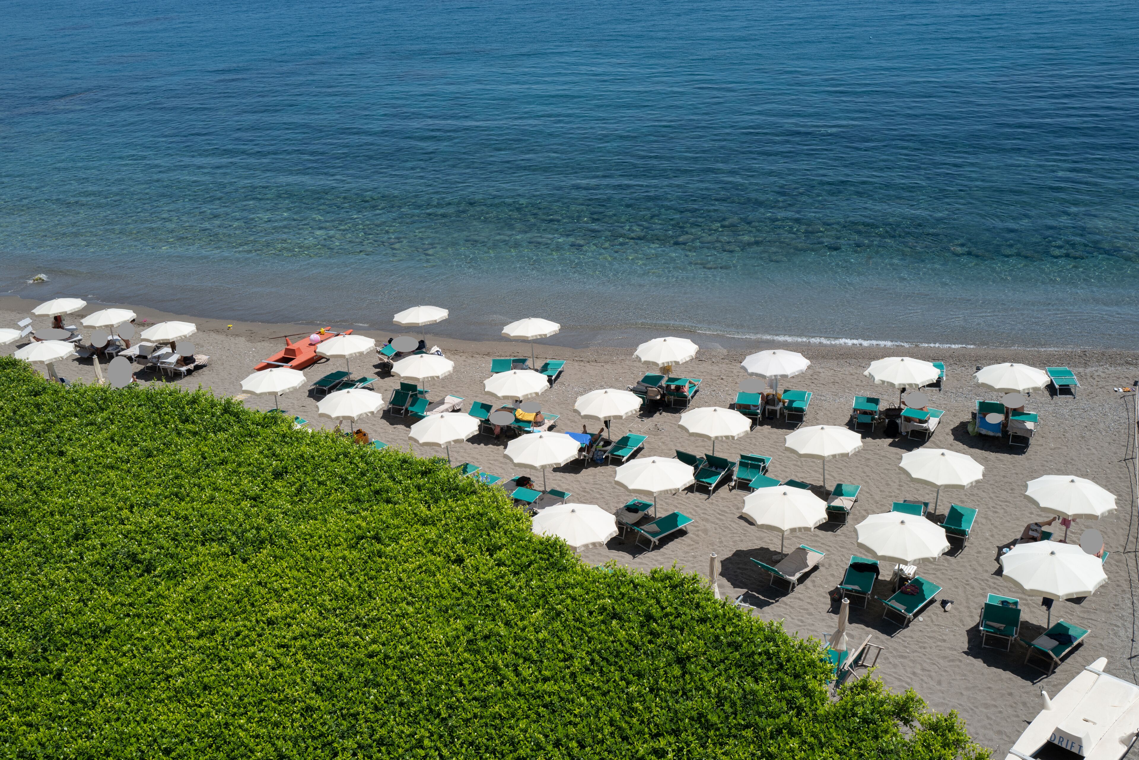A beach with rows of sun loungers and umbrellas, some with green canopies, and a clear view of the sea.