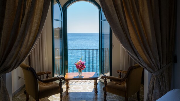 A room with a view of the sea through arched windows, a table with a vase of flowers, and two chairs. - Hotel Lido Mediterranee (Taormina)