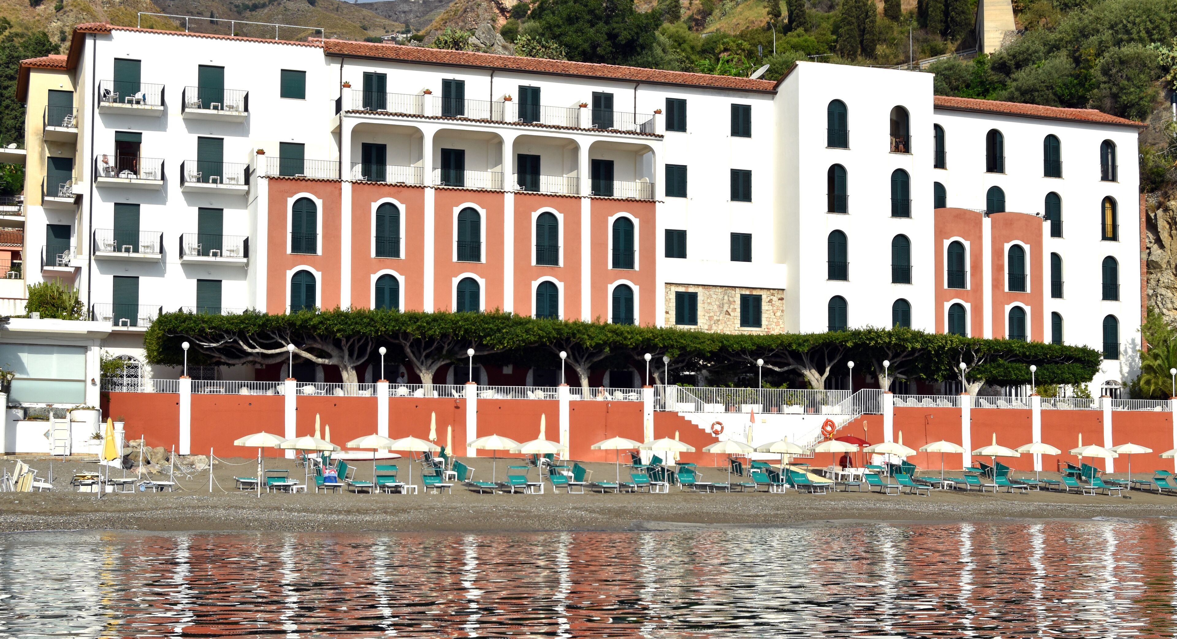 A coastal hotel with multiple floors, outdoor seating, and a view of the sea.