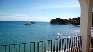 Une vue sur la côte, avec une balustrade de balcon, un yacht et une côte rocheuse bordée de bâtiments.