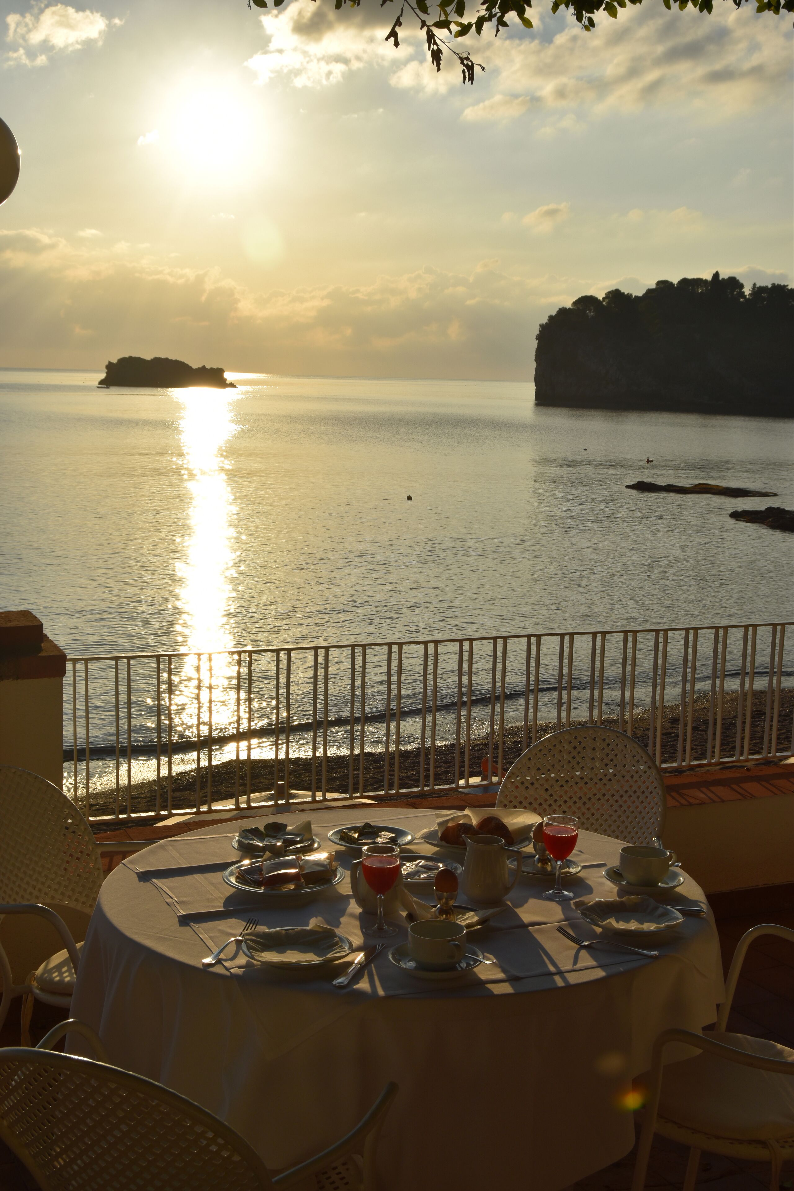 Une table dressée pour un repas, avec vue sur la mer et une île lointaine.