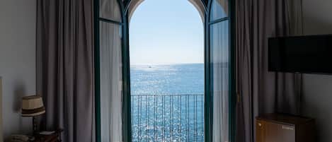 Una habitación con cama, escritorio, televisor y balcón con vista al mar.