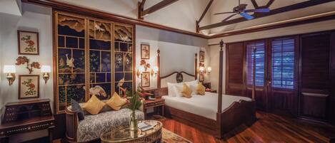 A traditional bedroom with a four-poster bed, a sitting area with a sofa and a coffee table, and a large window with decorative shutters.