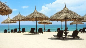 A beach with thatched umbrellas and wooden lounge chairs. - Furama Resort Danang (Da Nang)