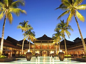 Un resort con piscina, palmeras y un edificio de varios pisos y balcones.