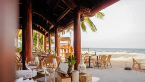 An outdoor dining area with tables and chairs, overlooking a beach and the ocean. - Furama Resort Danang (Da Nang)