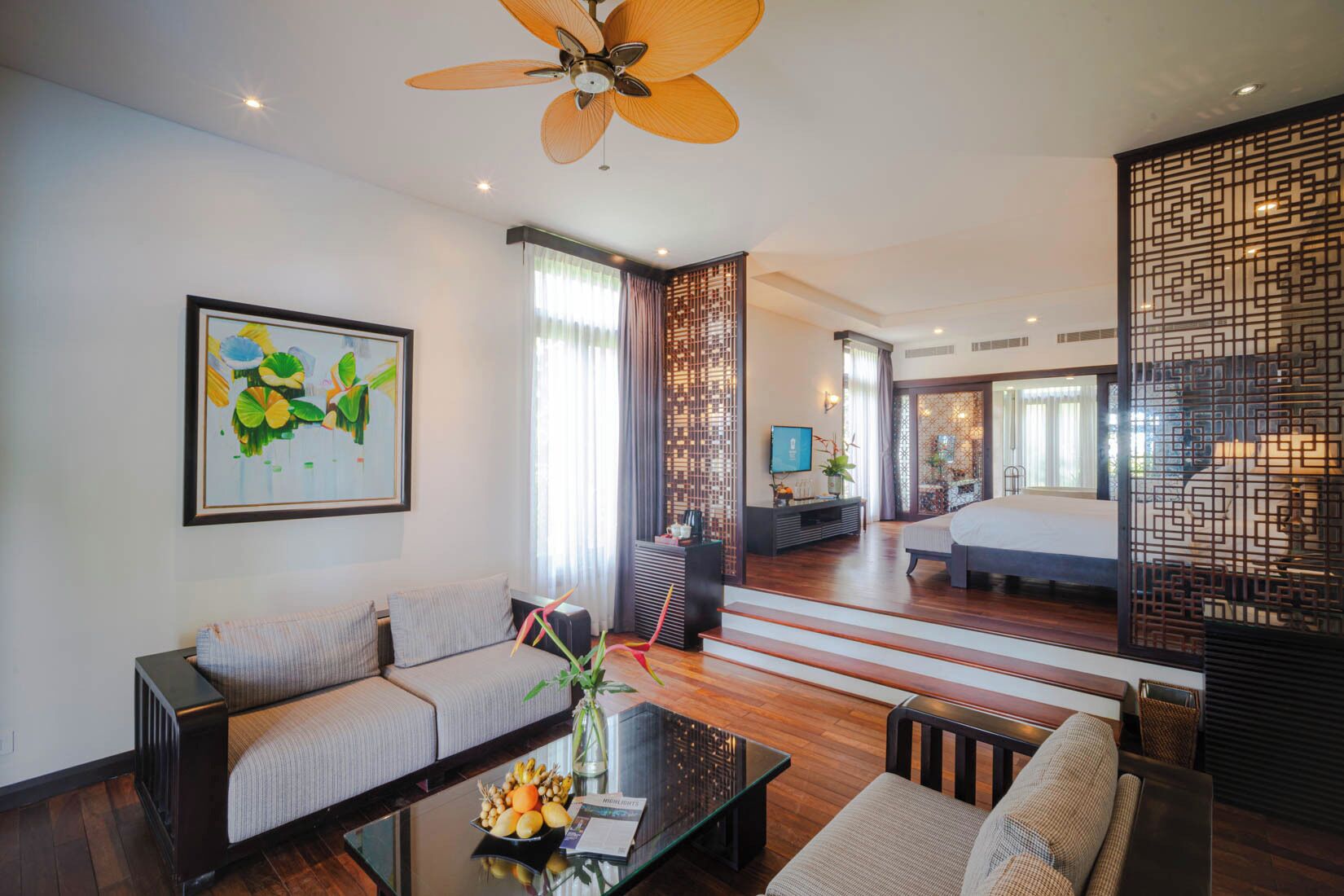 A modern hotel room with a sofa, coffee table, and a TV. There is a staircase leading to another room.