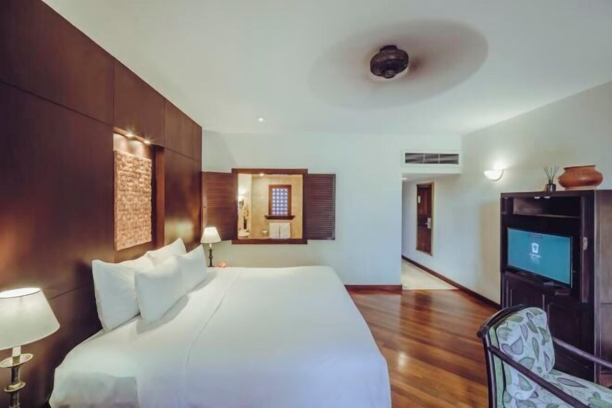 A hotel room with a large bed, a television, a mirror, and a wooden floor.
