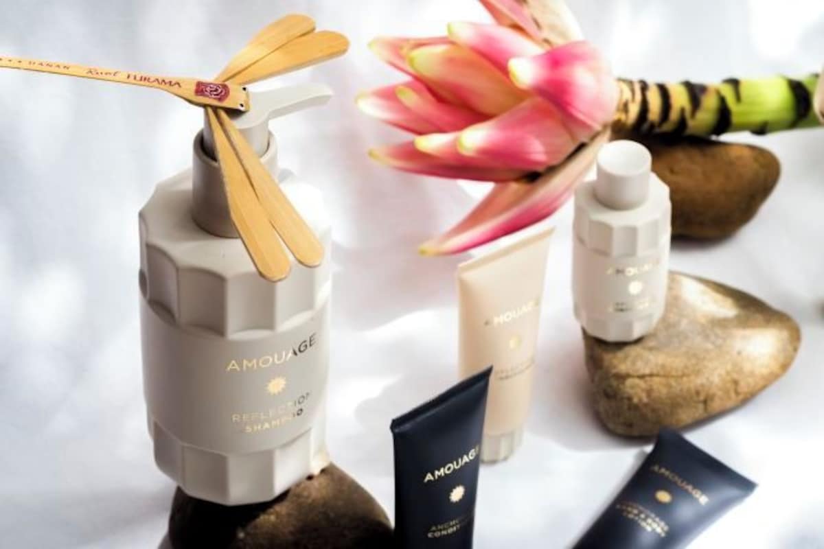 A collection of Amouage skincare products arranged on a surface with rocks and a flower.