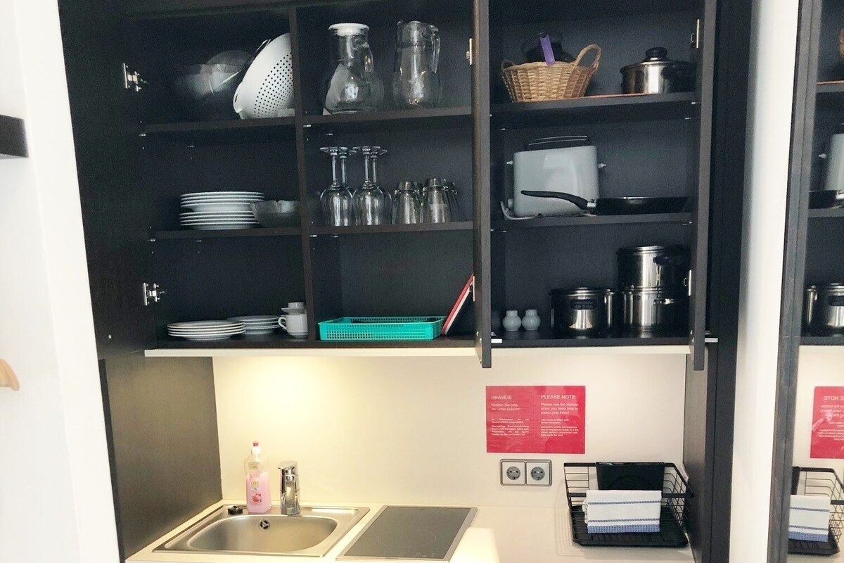 Cocina compacta con un lavamanos, una pequeña encimera y lavavajillas. Hay repisas arriba con varios utensilios de cocina.