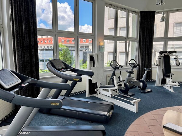 A gym with treadmills, stationary bikes, and weight machines, large windows with a view of buildings, and a blue carpeted floor. - Dorint Hotel Esplanade Jena (Jena)