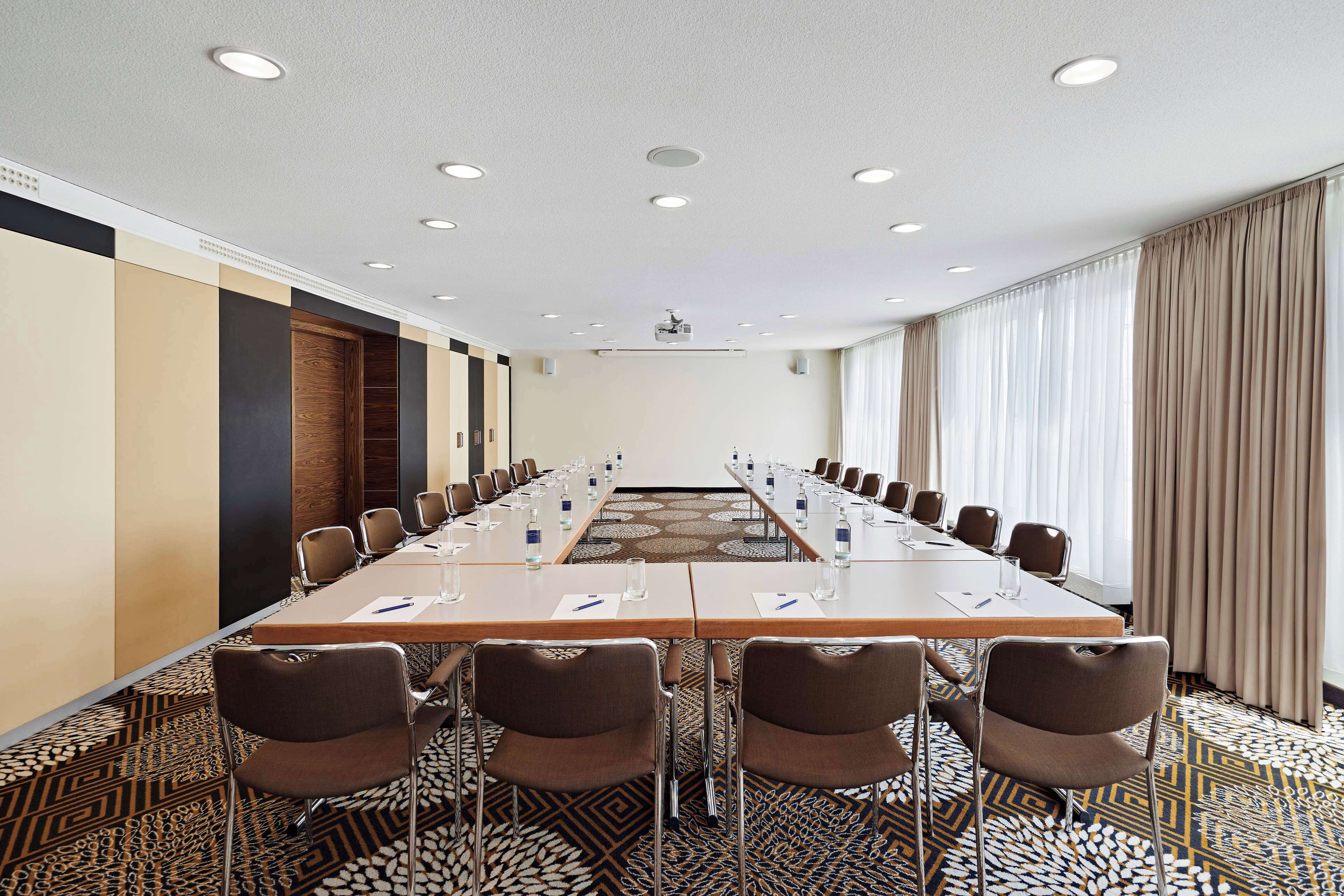 Un salón de conferencias con una larga mesa, sillas y una pantalla para proyector.