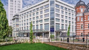 A modern hotel with a glass facade, multiple floors, and a prominent red brick building to the right. - Dorint Hotel Esplanade Jena (Jena)