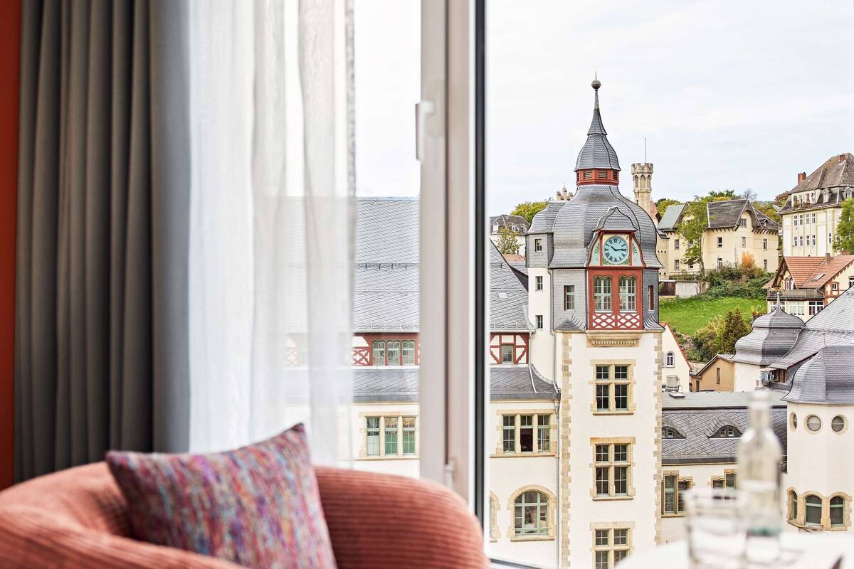 A hotel room with a large window offering a view of historic buildings and a clock tower.