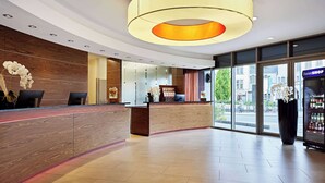A modern reception area with a wooden reception desk, a large circular light fixture, and a view of the street outside. - Dorint Hotel Esplanade Jena (Jena)