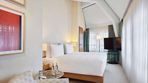 A hotel room with a large bed, a TV, a glass table with bottles, and a chair. - Dorint Hotel Esplanade Jena (Jena)