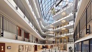 A spacious atrium with multiple levels, glass railings, and a central open area with tables and chairs. - Dorint Hotel Esplanade Jena (Jena)