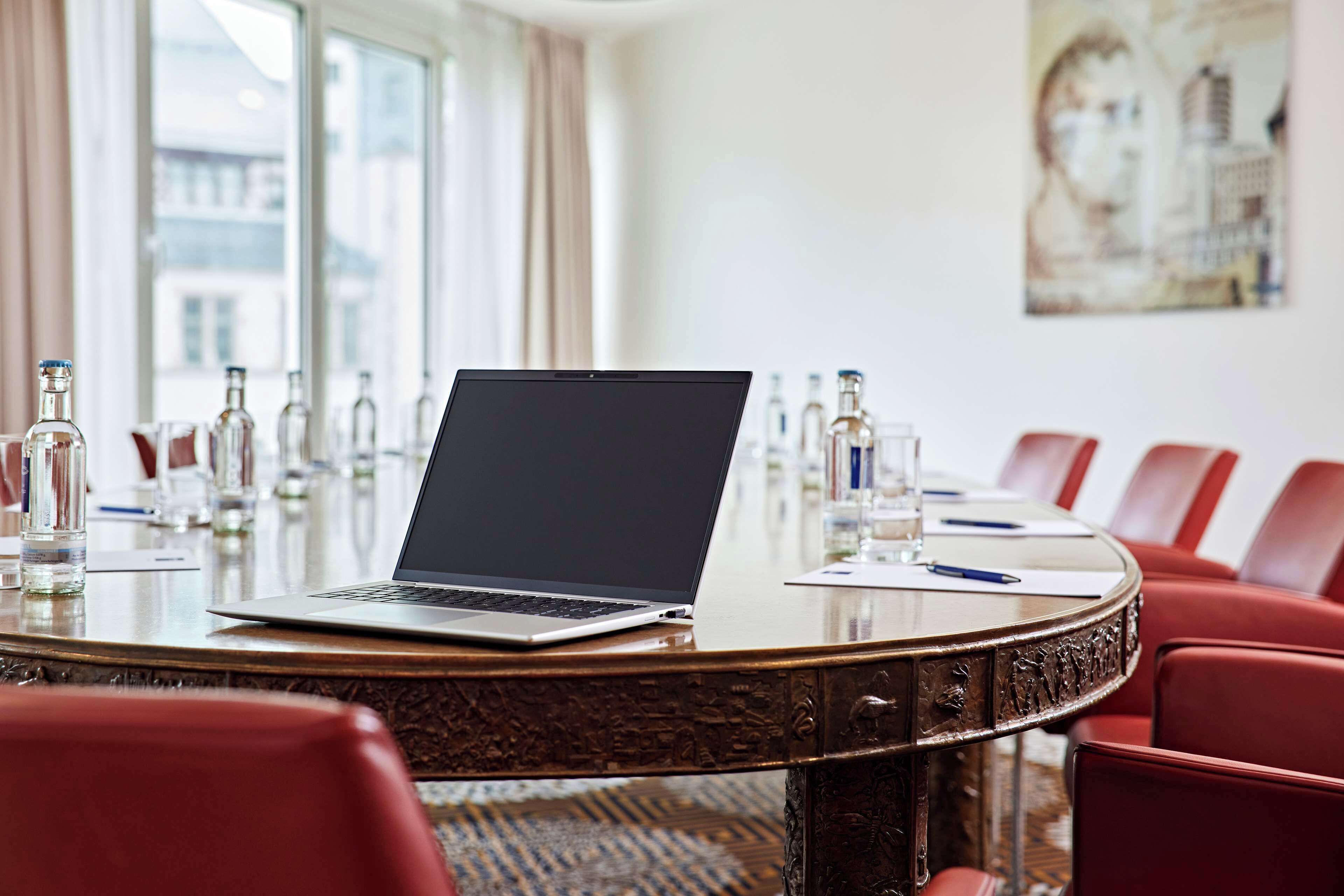 Une salle de conférence avec un ordinateur portable posé sur une table ronde, entourée de chaises rouges, et des bouteilles et des verres sur la table.