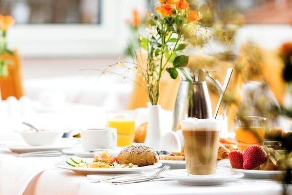 A breakfast table with a coffee cup, croissant, strawberries, and a vase of flowers. - Dorint Hotel Esplanade Jena (Jena)