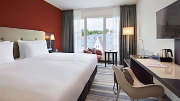 Habitación de hotel con una cama grande, un escritorio, una silla, una mesita y vistas a edificios por la ventana.