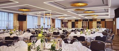 A banquet hall with round tables, white tablecloths, and candle centerpieces.