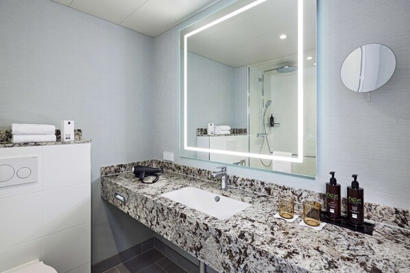 Un baño moderno con encimera de granito, un espejo grande y un cabezal de ducha de mano.