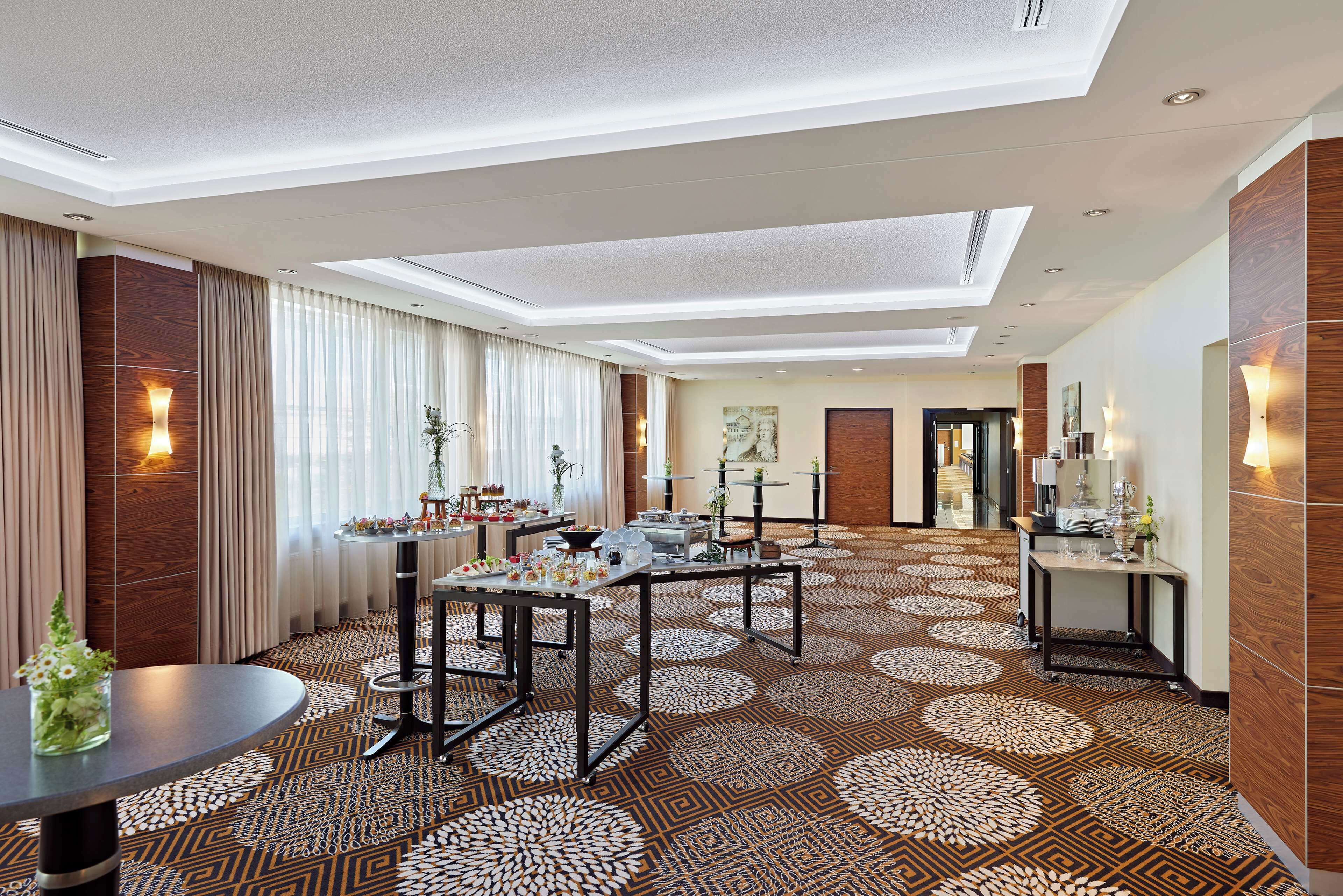 Un hall d’hôtel spacieux, doté d’un tapis à motifs, de nombreuses tables et d’un design de plafond moderne.