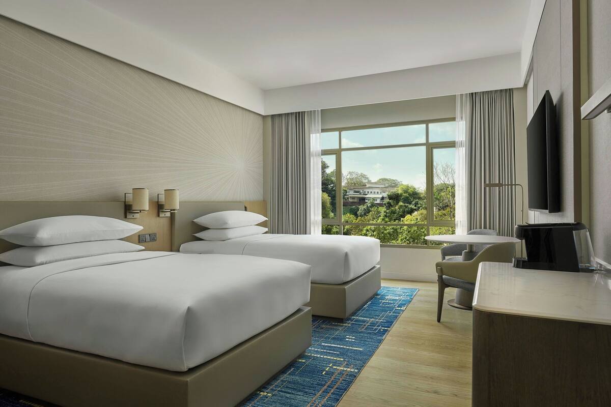 Hotelkamer met twee bedden, een bureau, een stoel, een televisie en een groot raam met uitzicht.