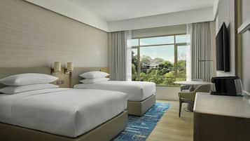 A hotel room with two beds, a desk, a chair, a TV, and a large window with a view.