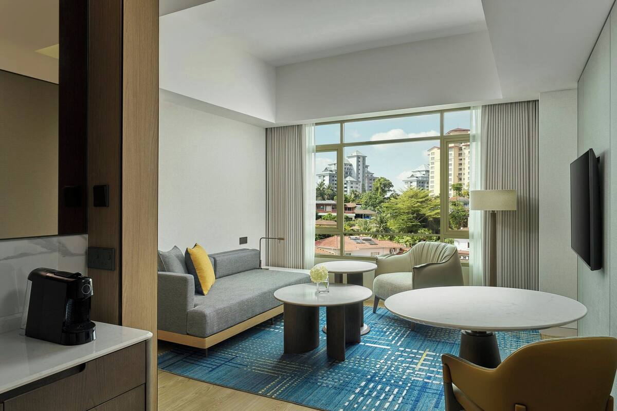 Een moderne hotelkamer met een bank, twee ronde tafels, een koffiezetapparaat en een televisie.