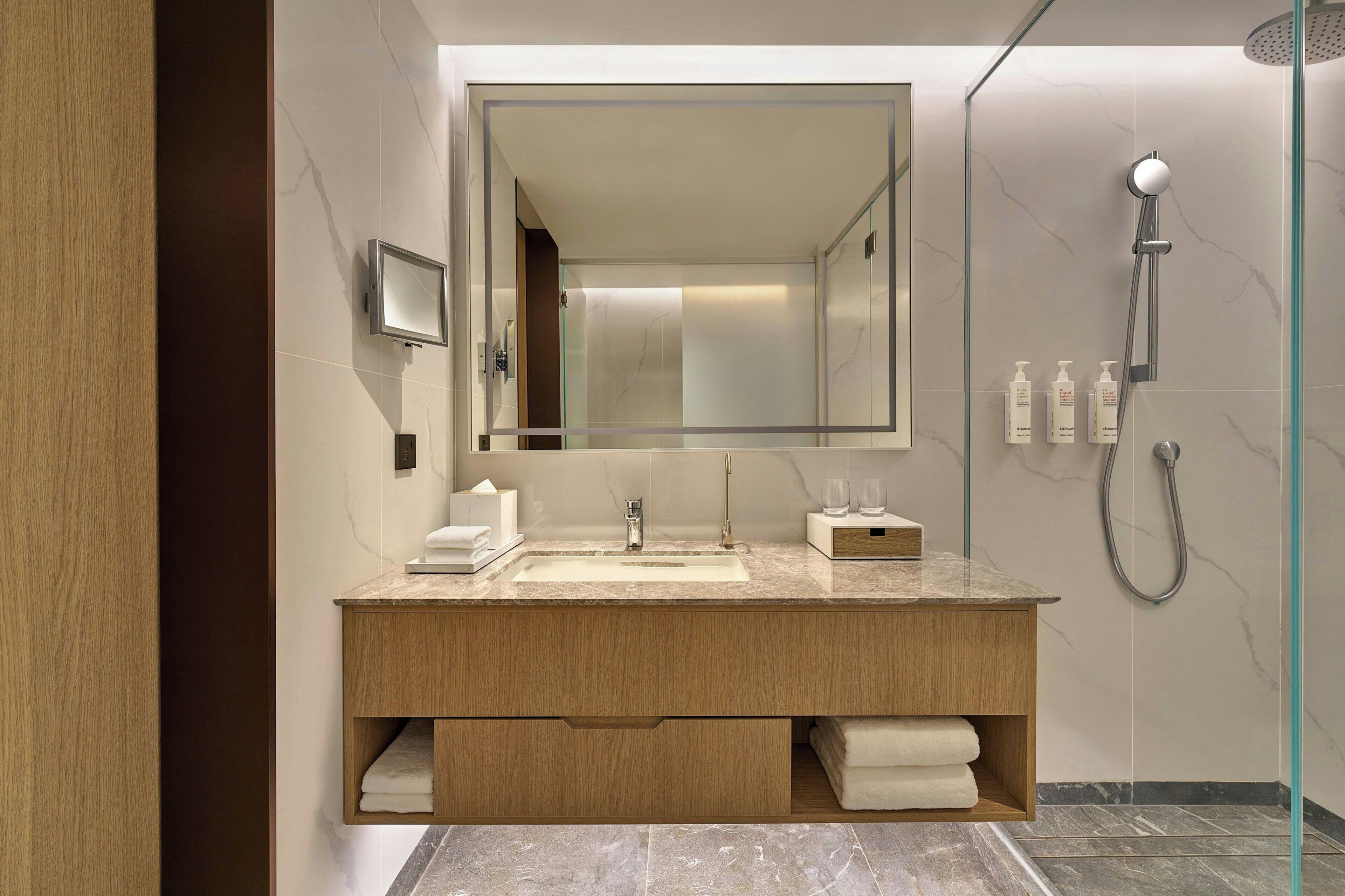 A modern bathroom with a large mirror, a sink, a shower, and a wooden vanity.