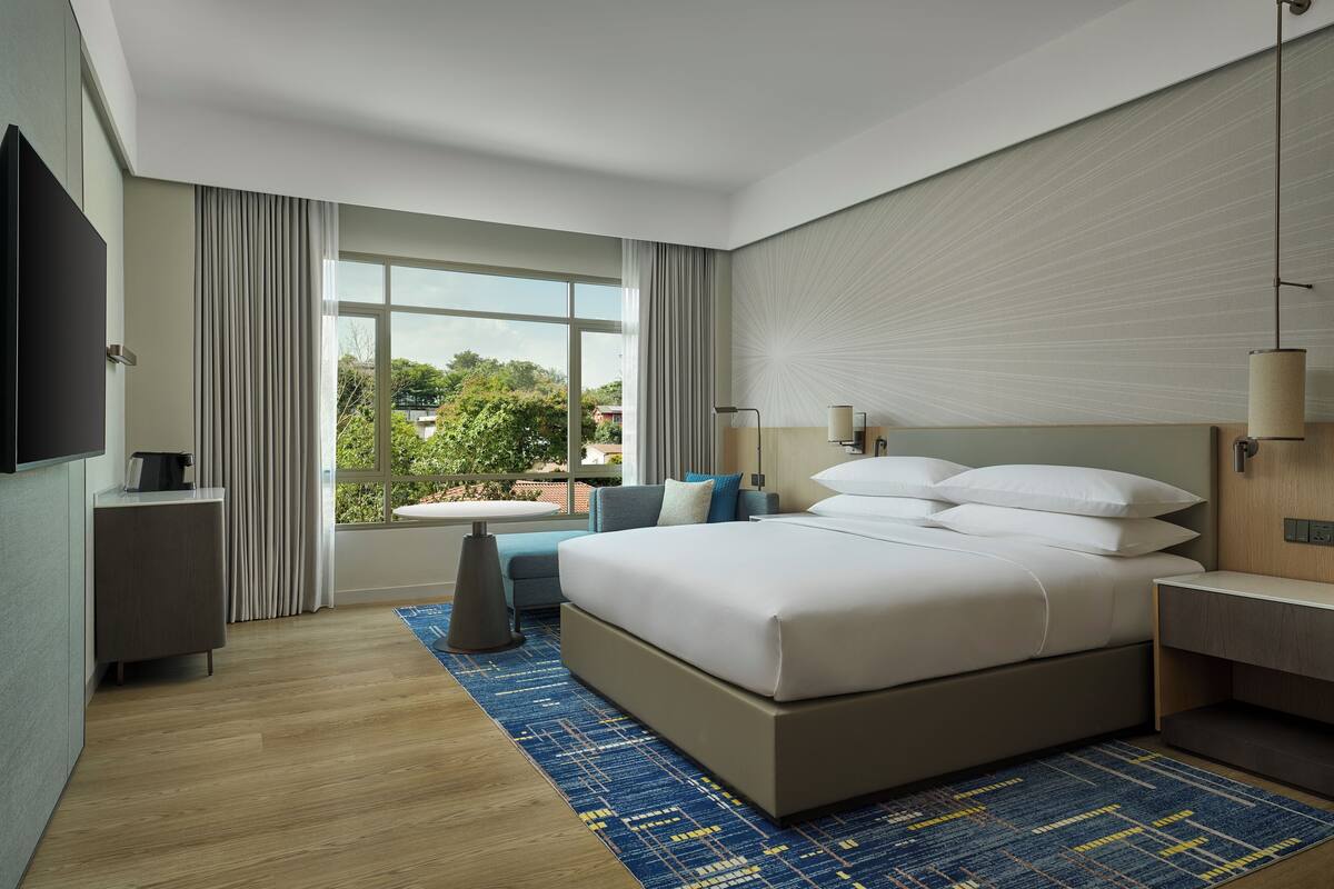 Een moderne hotelkamer met een groot bed, een bureau, een stoel, een televisie en een raam met gordijnen.