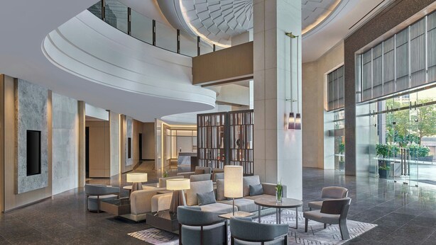 A spacious lobby with a high ceiling, a central seating area with sofas and armchairs, a coffee table, and a large window offering a view of the outdoors. - Petaling Jaya Marriott Hotel (Petaling Jaya)