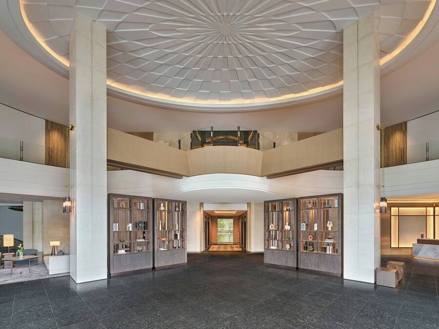 A spacious lobby with a high ceiling, a central staircase, and a reception desk.